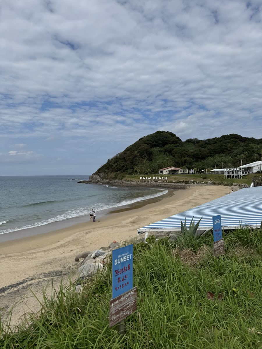 A quiet sandy beach in Itoshima with a green headland and a "Palm Beach" sign