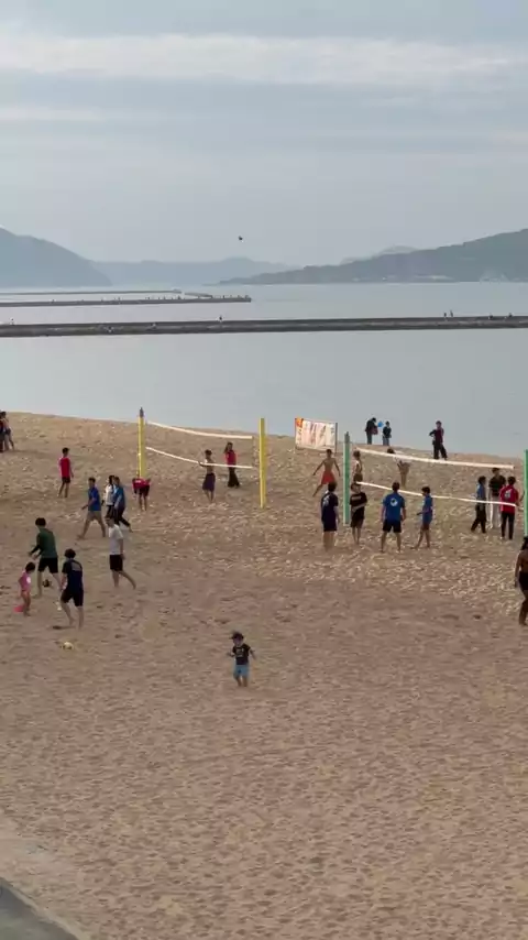 People playing beach volleyball at Momochi beach in the late afternoon, with islands in the bay behind