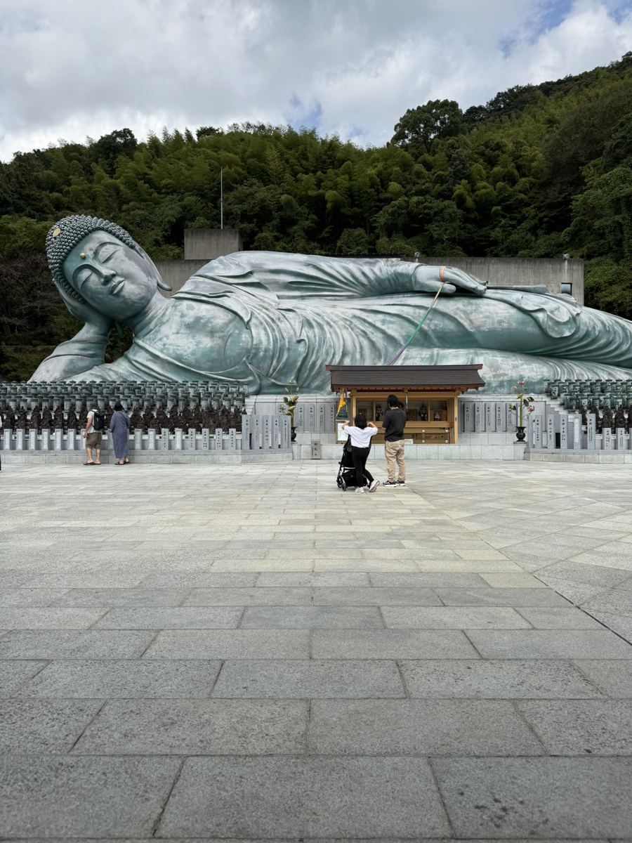 The giant bronze reclining Buddha at Nanzoin with a small shrine and visitors in front