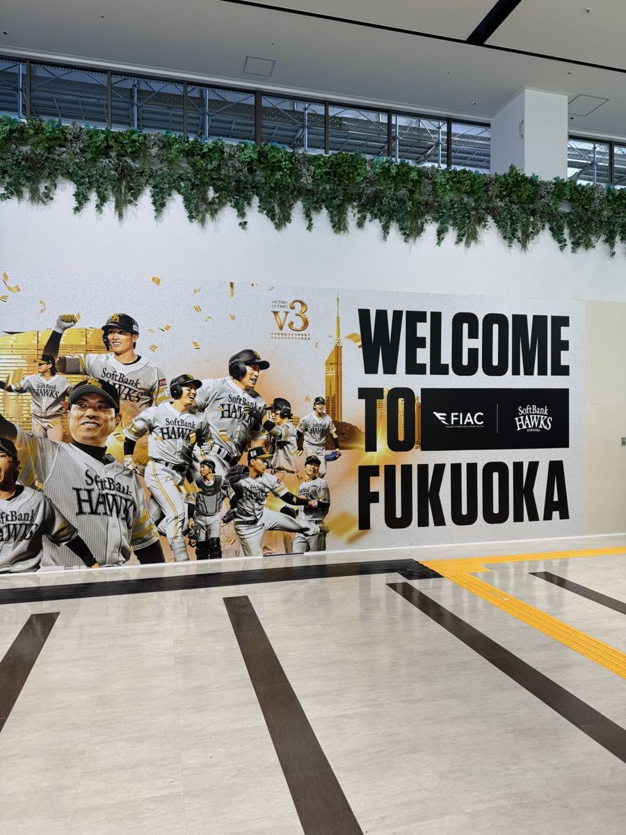 A large SoftBank Hawks "Welcome to Fukuoka" banner in the airport arrivals hall